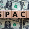 SPACs symbol. Wooden cubes with words 'SPACs, special purpose acquisition companies' on beautiful background from dollar bills, copy space. Business and SPACs concept.