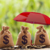 Risk protecting, wealth management and long term money investment, financial concept: Arrange coins and US dollar bag Under the red umbrella. Depicts asset security for sustainable growth.