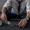 businessman with drug addiction pouring pills on table from bottle