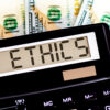 Calculator with text ETHICS on dollars. Business, finance conceptual.