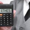 ETHICS word text inscription on calculator in a male hand of a businessman in white shirt and blue tie, Concept of finance and banking. close up, banner.